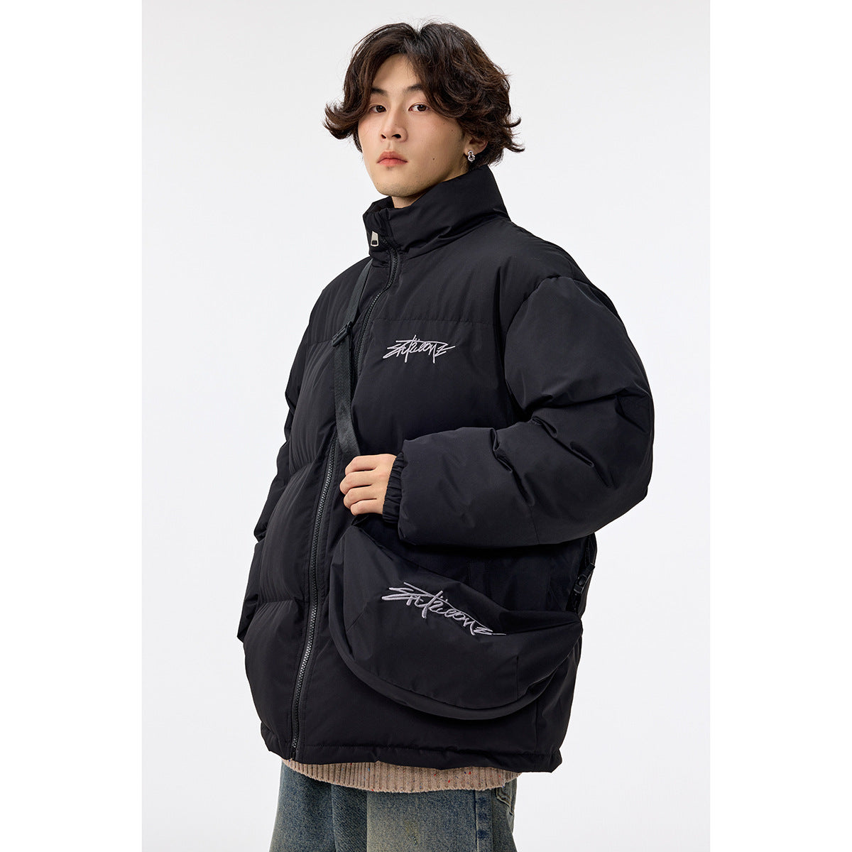 Man in a black puffer jacket with a high collar, shown at an angle with a matching crossbody bag.