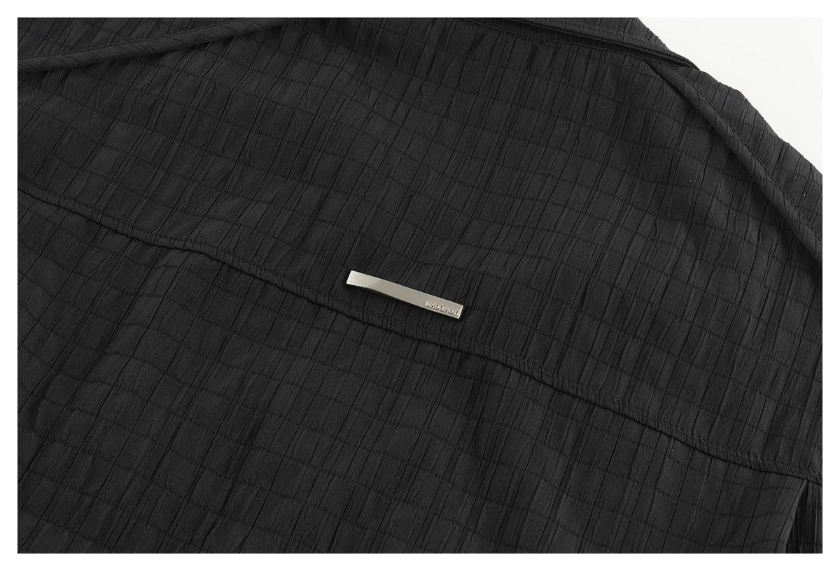 Close-up of black textured fabric with a stitched panel seam and a small silver metal plaque.
