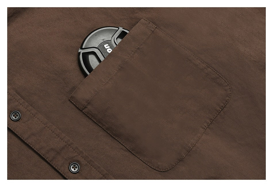 Close-up of a brown shirt’s chest pocket and placket, with part of a dark round object tucked inside.