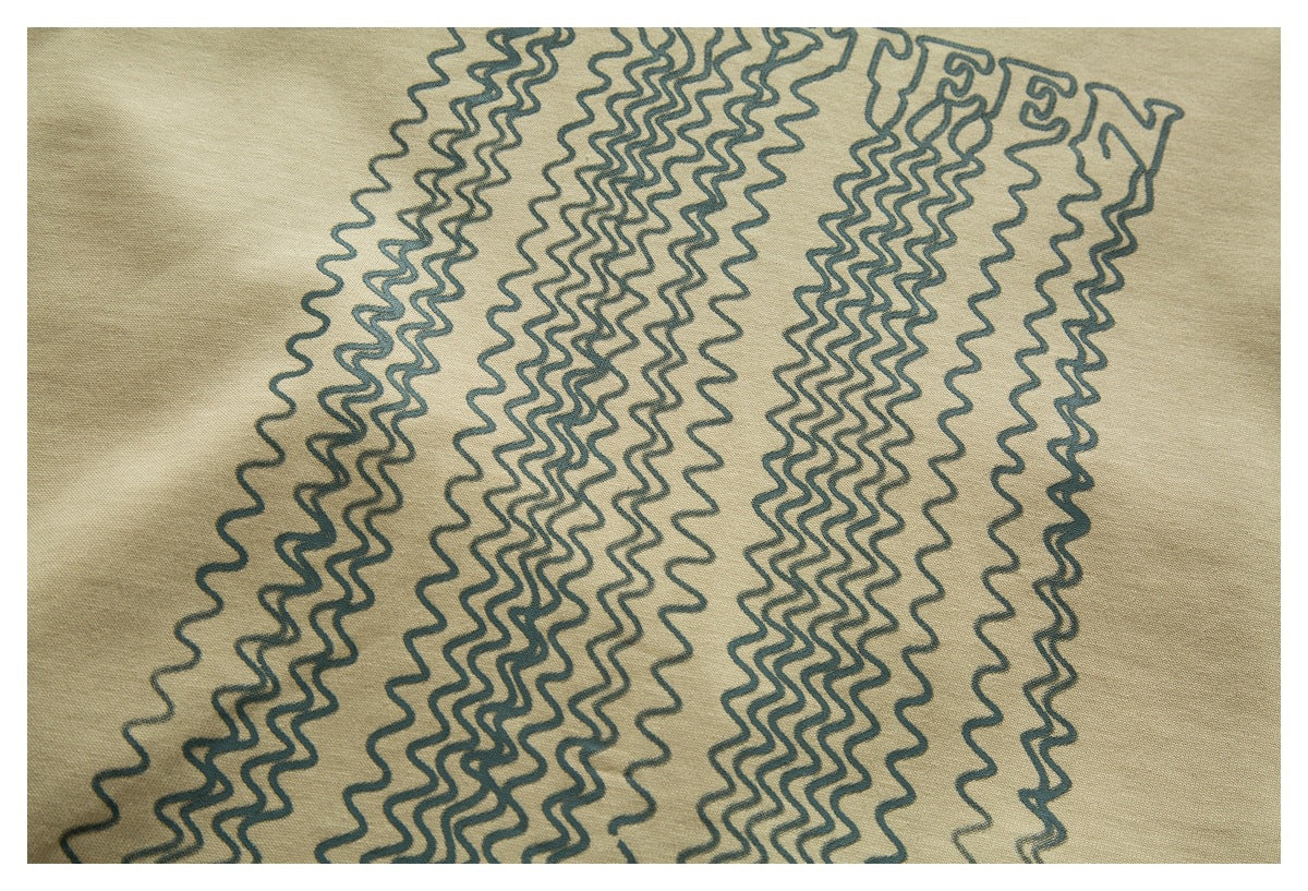 Close-up of dark wavy lines and partial lettering printed on beige T-shirt fabric.