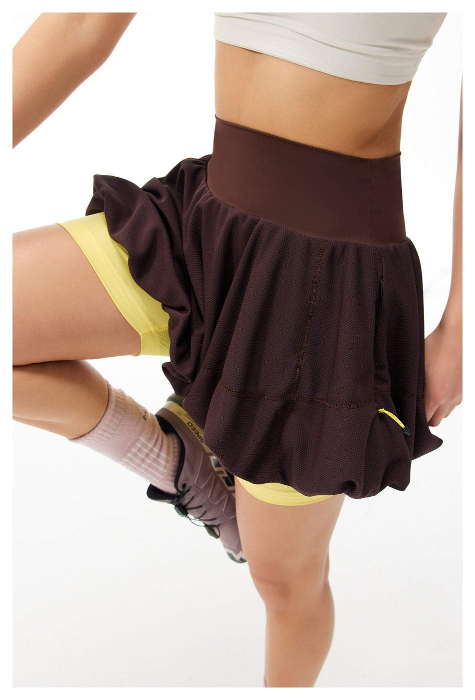 Close-up of a dark brown bubble tennis skirt with a wide waistband, yellow built-in shorts, and a small side pocket zipper.