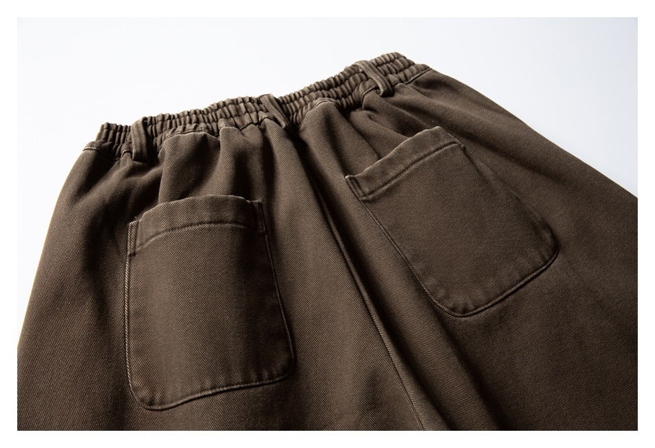 Close-up of brown trousers with a gathered elastic waistband and two patch pockets.