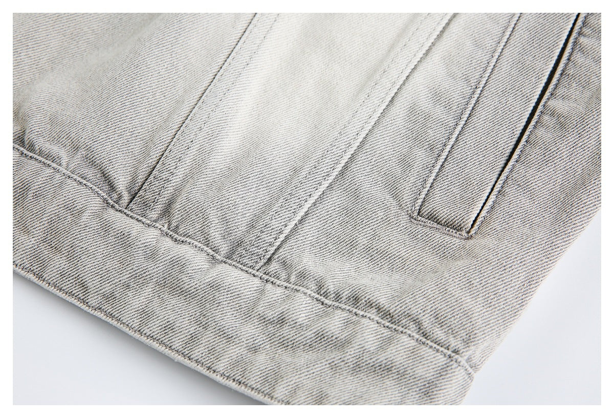 Close-up of light gray denim with a stitched hem and pocket edge.