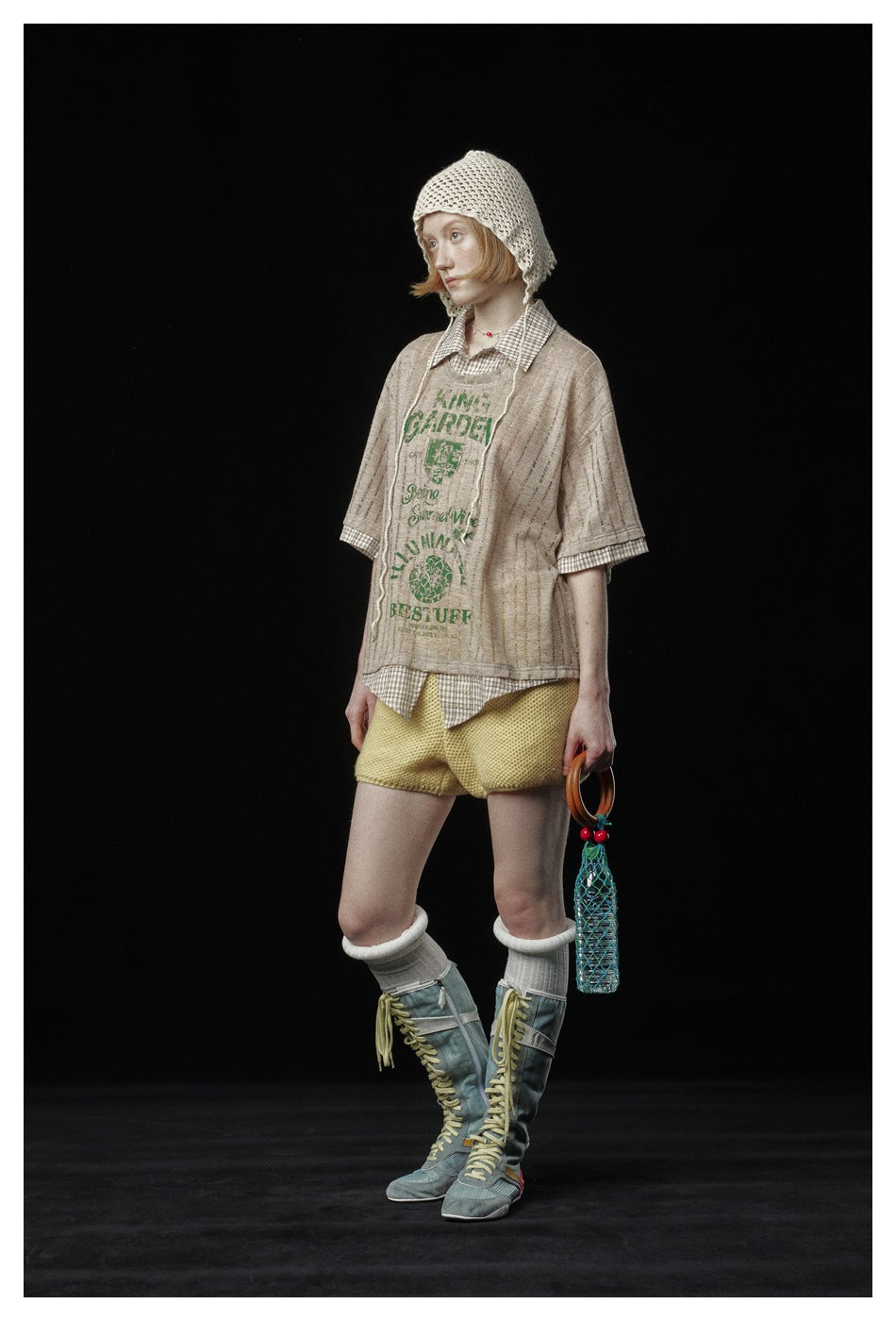 Model in three-quarter view wearing the brown striped layered top with green graphic and plaid trim