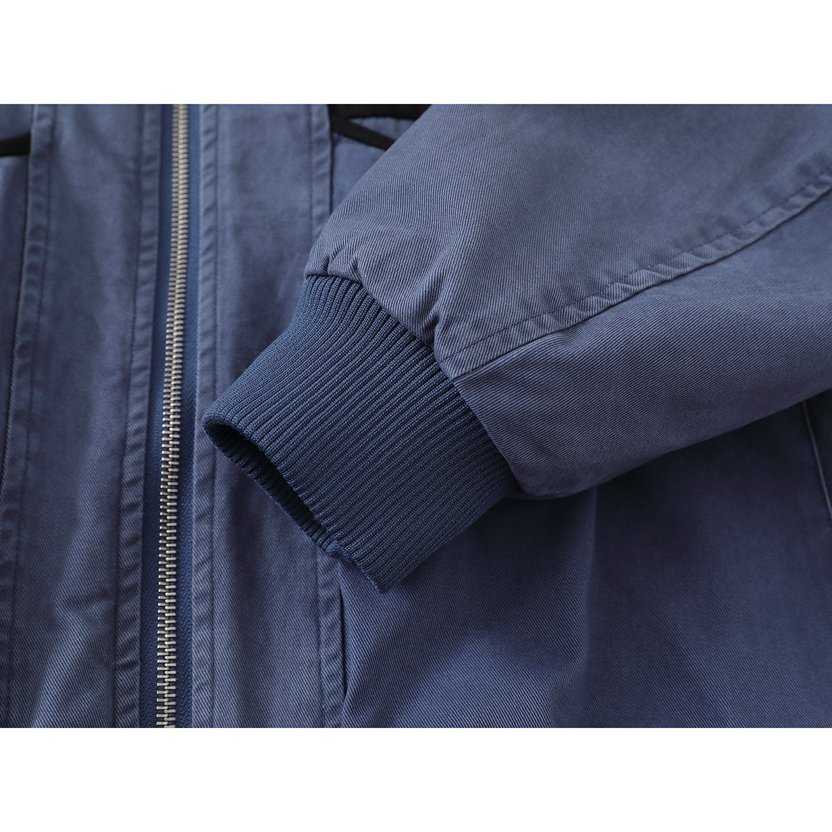 Close-up of a blue jacket sleeve with a dark ribbed cuff beside the front zipper.