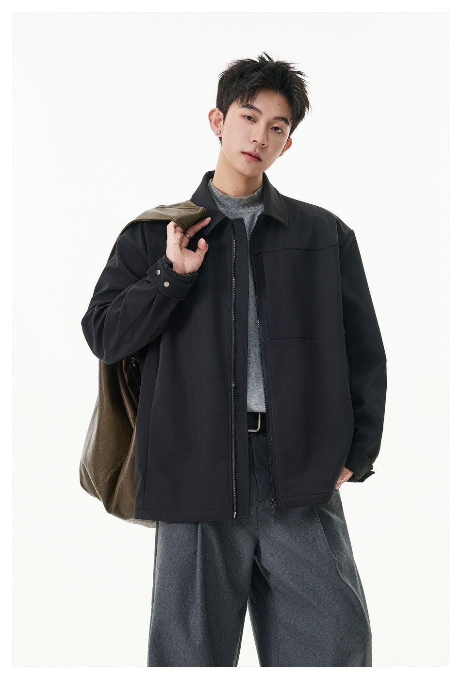 Model wearing a black zip-front jacket with a pointed collar and buttoned cuffs; a brown jacket is draped over his shoulder.
