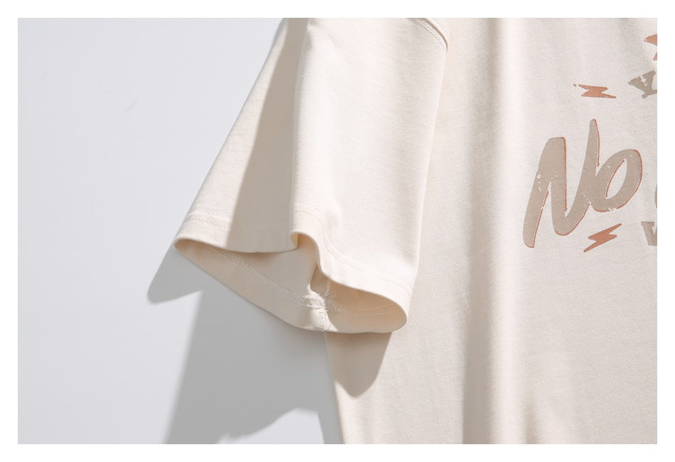 Close-up of the cream T-shirt’s short sleeve, hem stitching, and a cropped edge of the chest graphic.
