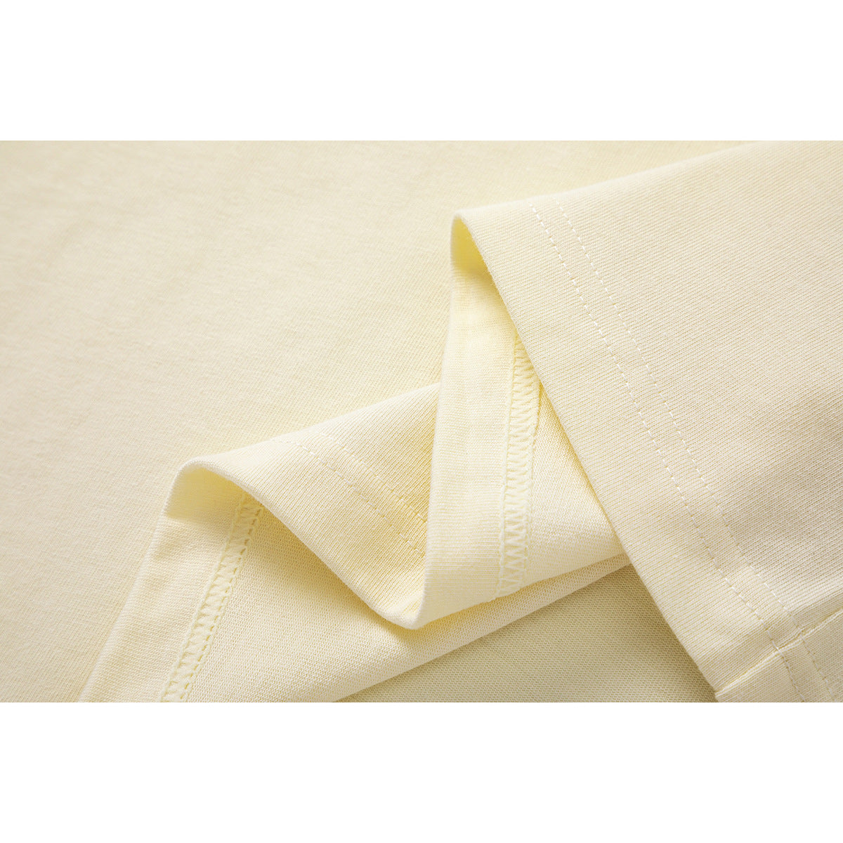 Close-up of cream T-shirt fabric folded to show the stitched hem and seam finish.