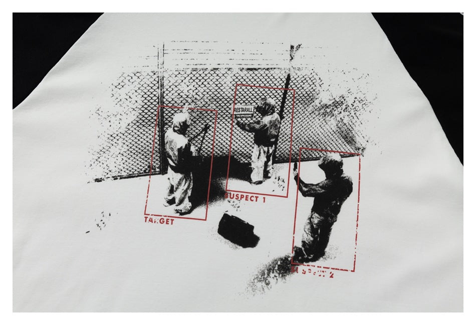 Close-up of a white garment with a black graphic of figures by a fence and red outlined labels.