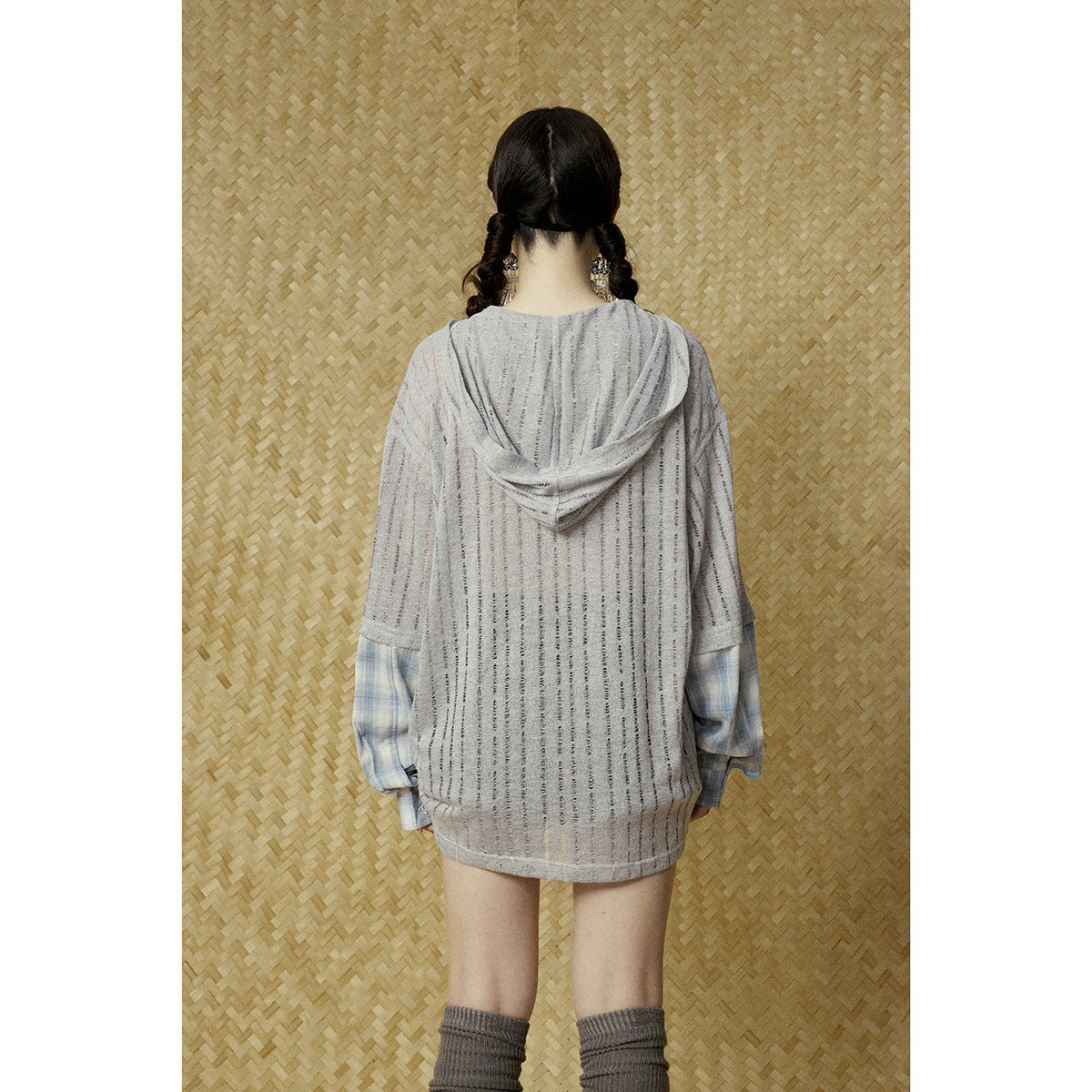 Back view of a gray striped hooded top with a draped hood and blue plaid sleeves, worn by a model.