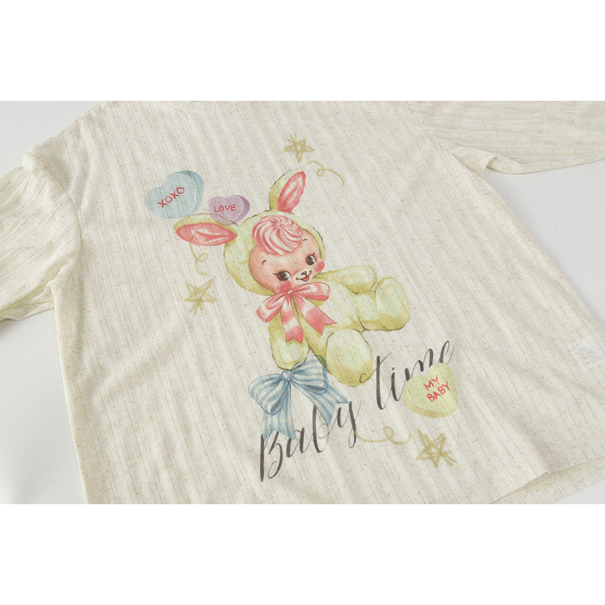 Ivory short-sleeve shirt laid flat, with a pastel bunny, bows, stars and English lettering on the front.