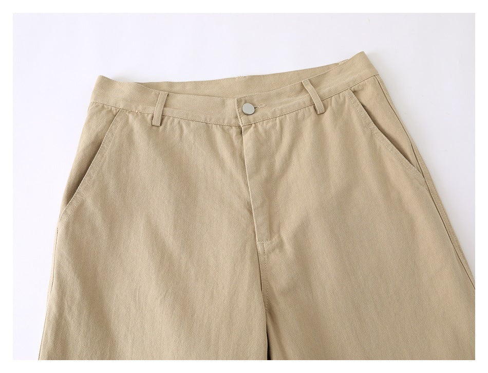 Close view of the front waist and upper legs of beige pants, showing the button, belt loops, and slanted pockets.