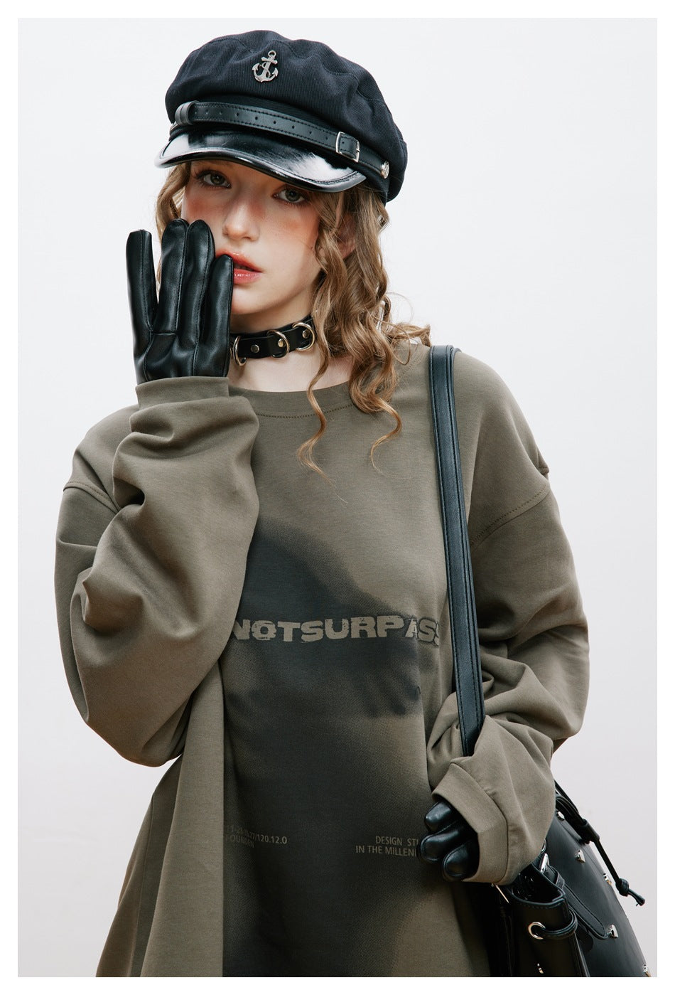 Close-up of model in a gray-green graphic sweatshirt with a cap, choker, black glove and shoulder bag