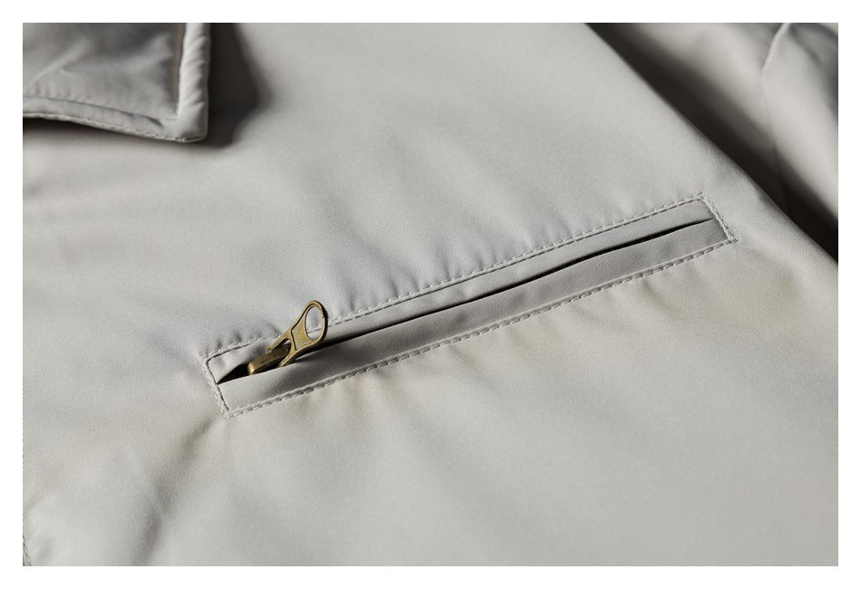Close-up of a light gray jacket with a diagonal welt pocket and brass-colored zipper pull.