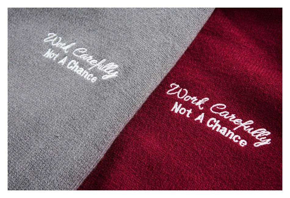 Close-up of gray and dark red knit cardigans with white embroidered text reading “Work Carefully Not A Chance.”