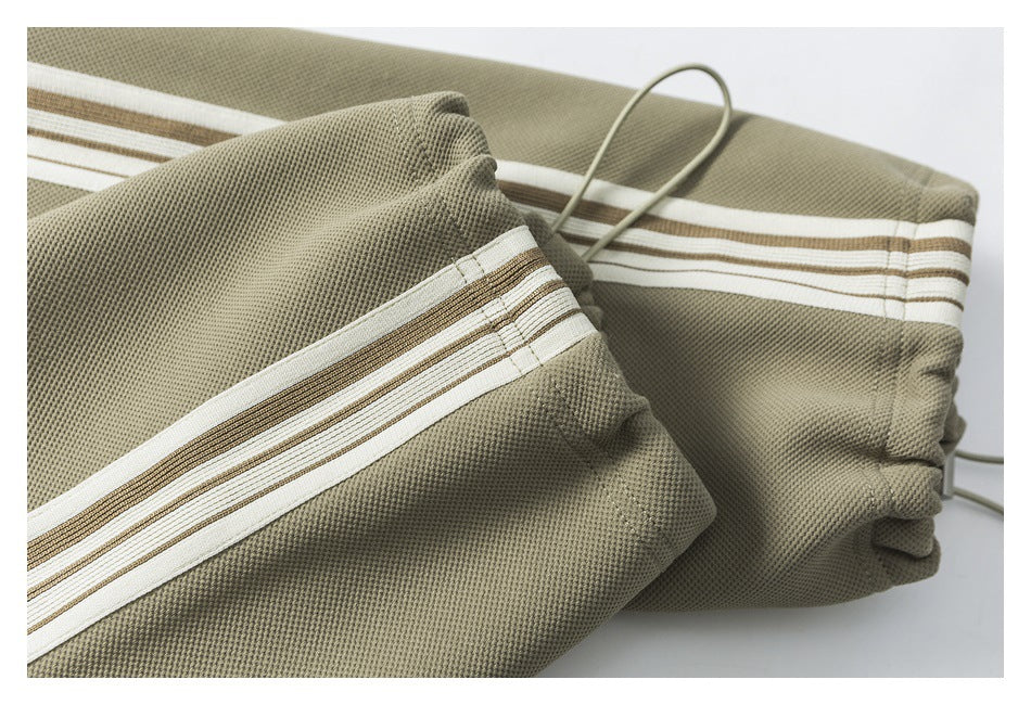 Close-up of olive-gray pants fabric with a cream and brown striped trim.