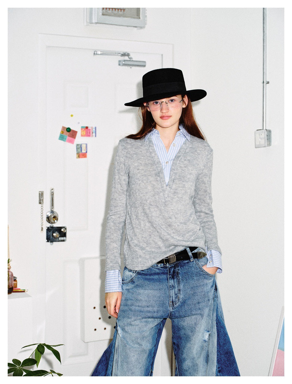Model wearing a light gray V-neck sweater over a blue striped shirt, paired with wide-leg jeans and a black hat.