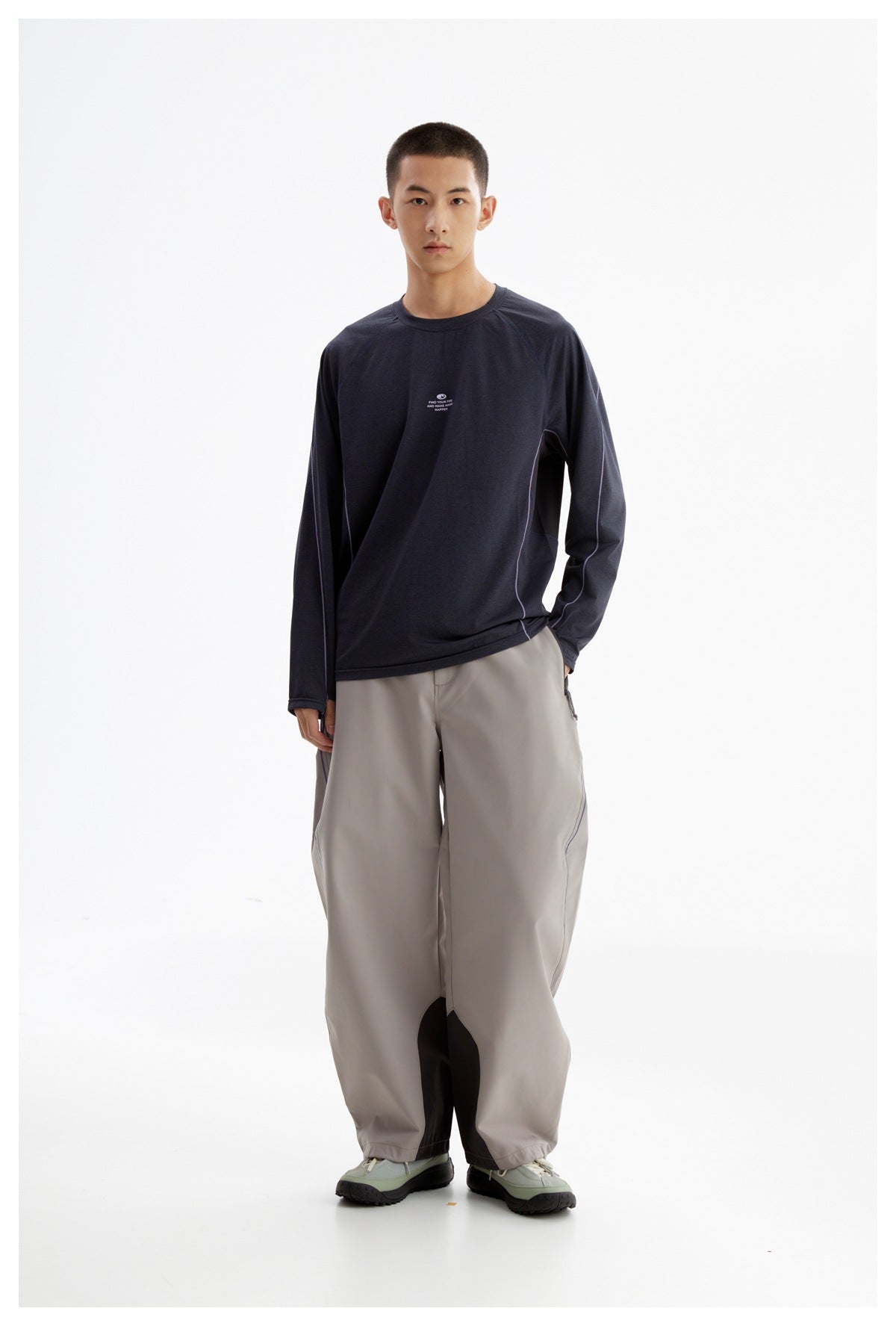Full-length front view of a man wearing a dark navy long-sleeve shirt with light piping and wide gray trousers.