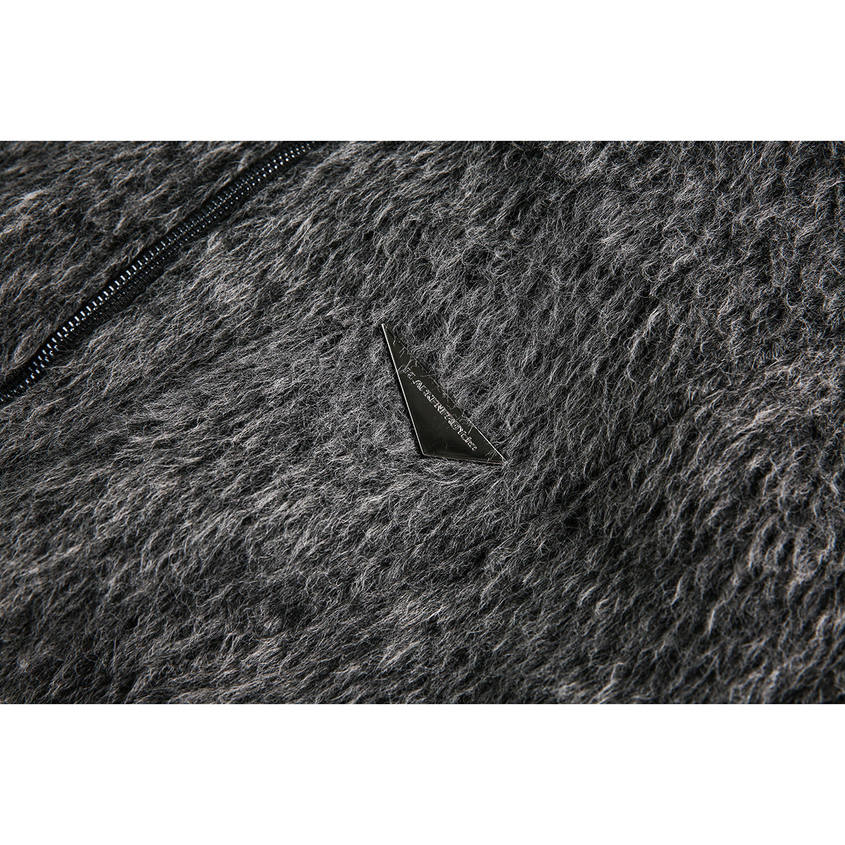 Close-up of a small black triangular plaque on the dark gray fuzzy jacket beside a zipper.