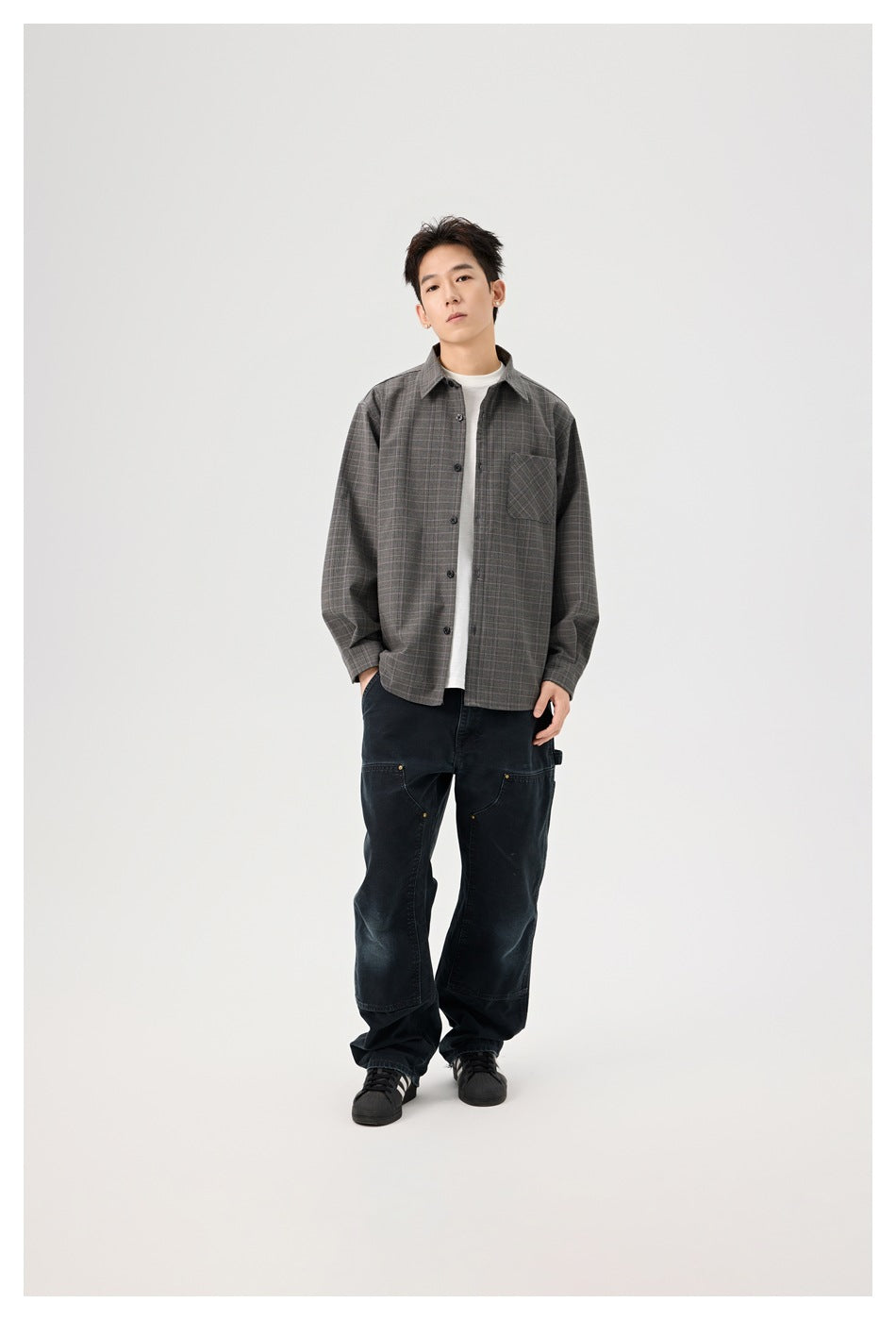 Full-length front view of a model wearing a gray plaid overshirt, white tee, loose black pants, and black sneakers.