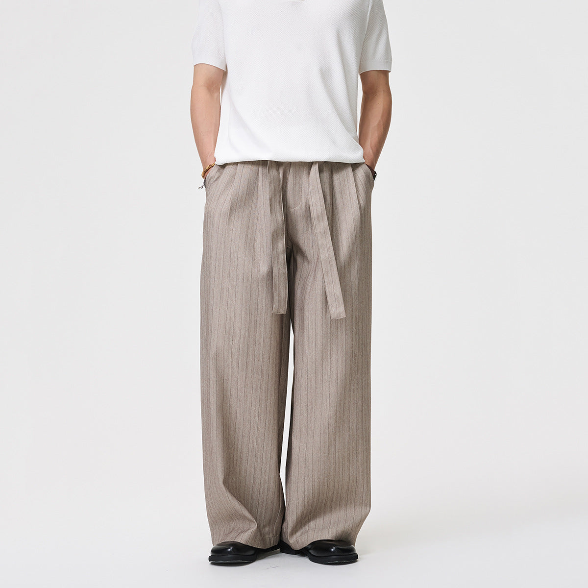 Front view of a model wearing wide-leg taupe-gray pinstriped trousers with a long waist tie.