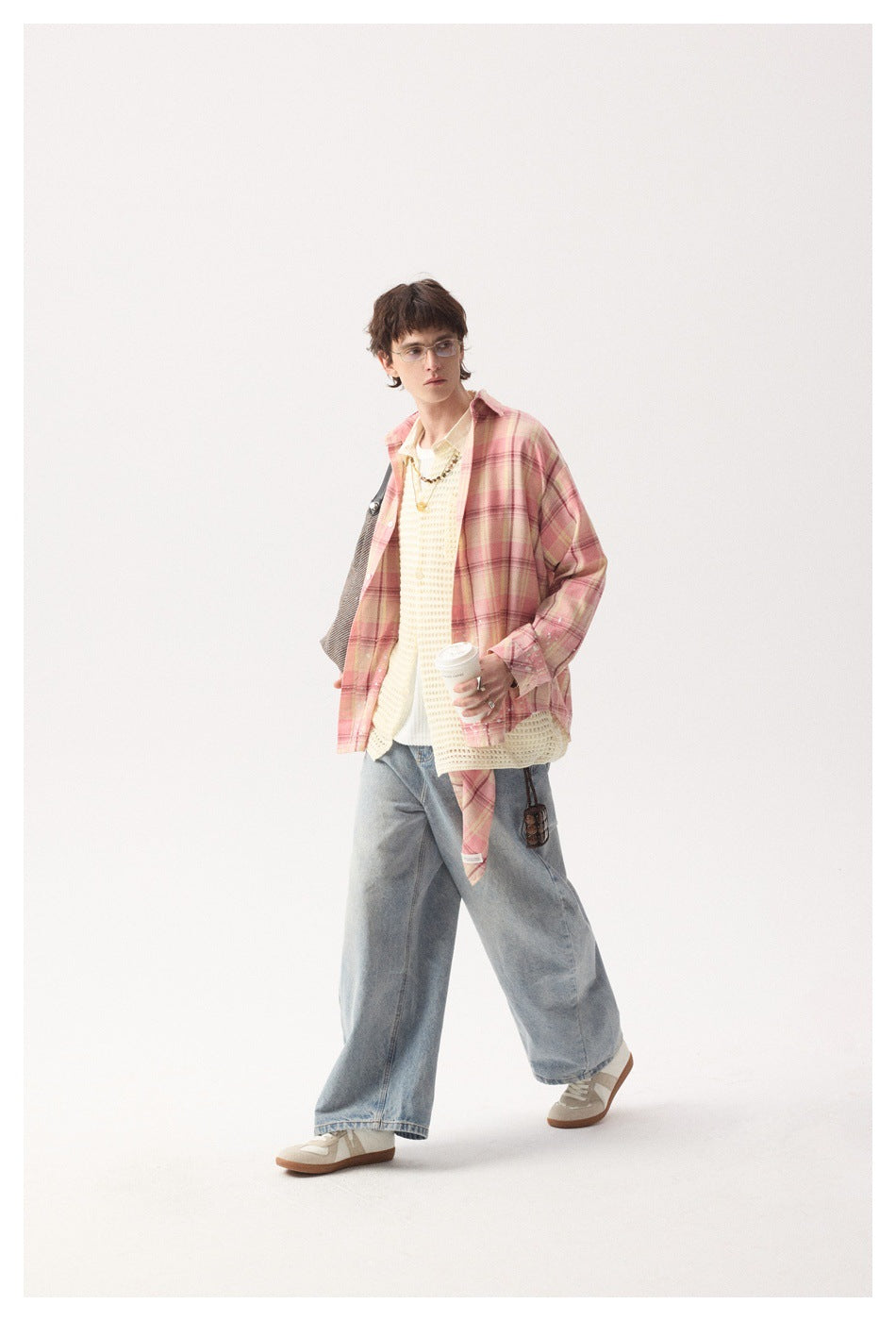 Full-length model wearing a pink plaid overshirt with cream knitwear and loose light-wash jeans.