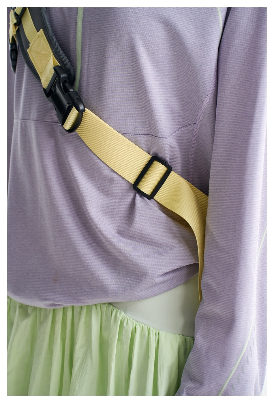 Close-up of the lilac top's front pocket and sleeve beside a yellow backpack strap and the mint skirt waistband.