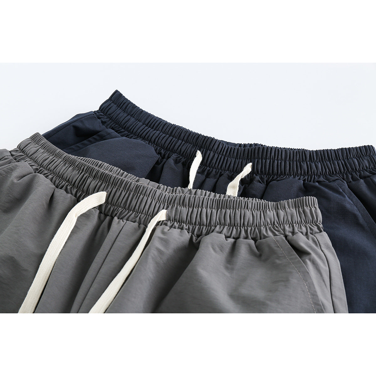 Close-up of gray and navy shorts with gathered elastic waistbands and white drawstrings.