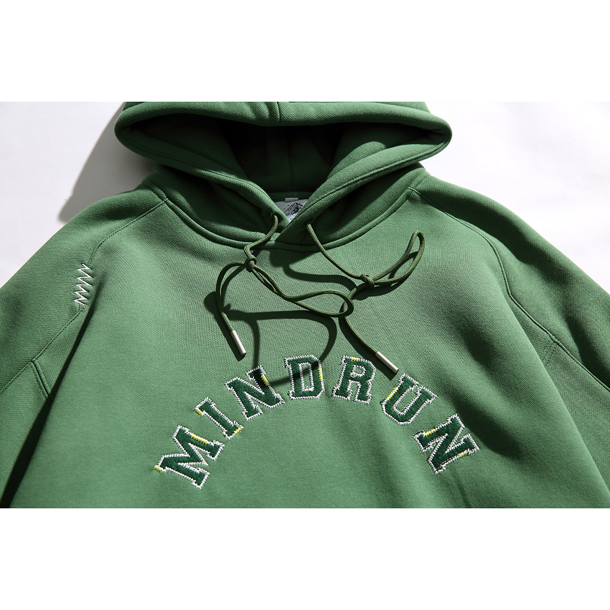 Close-up of a green hoodie showing its hood, drawstrings, sleeve stitching and embroidered MINDRUN chest lettering.