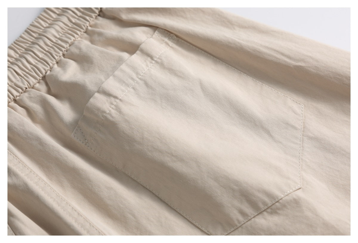 Close-up of beige trousers showing a large stitched patch pocket beneath the elastic waistband.