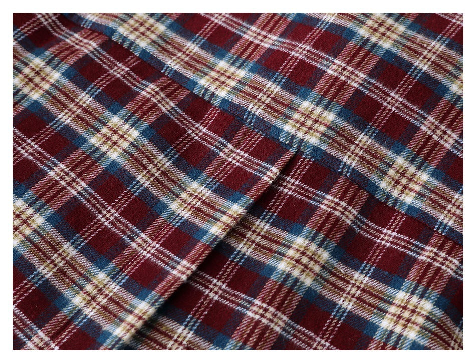Close-up of the overlapping front placket on a burgundy, navy, cream, and tan plaid shirt.