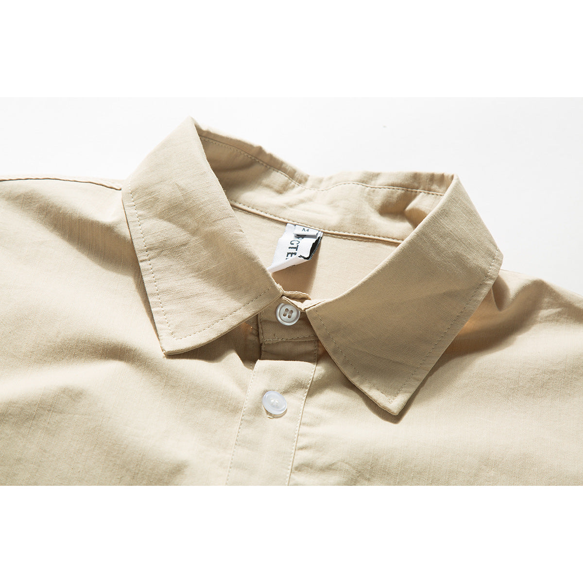 Close-up of a beige short-sleeve shirt’s pointed collar, top buttons and inner neck label.