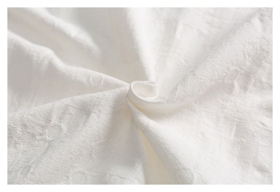 Close-up of ivory-white fabric gathered into soft folds, showing a fine textured weave.