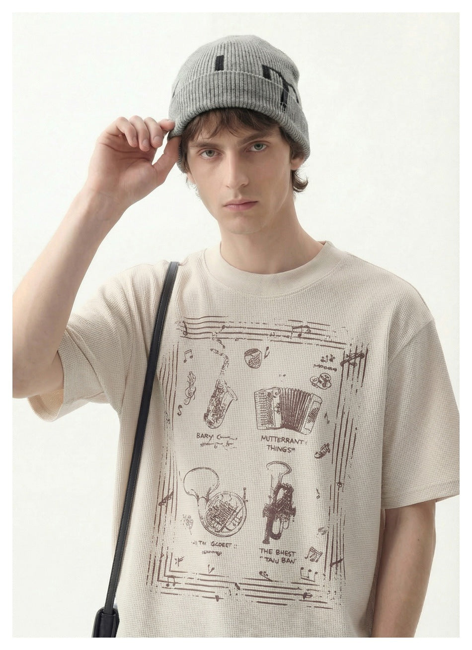Close-up of a model in a beige waffle-knit T-shirt with an instrument graphic, wearing a gray beanie
