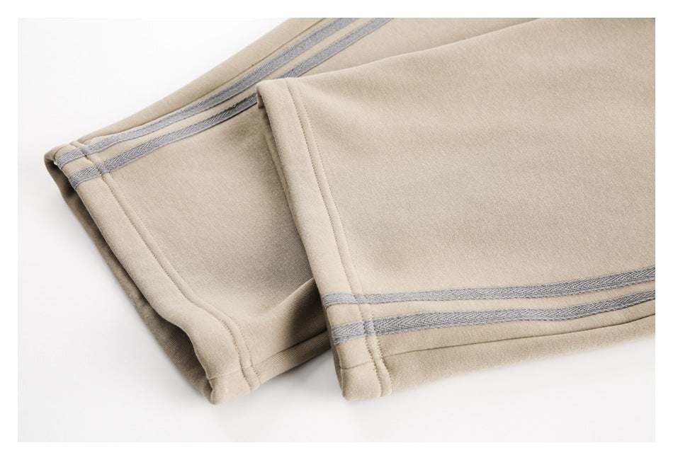 Close-up of beige pants with folded leg hems edged by gray decorative bands.