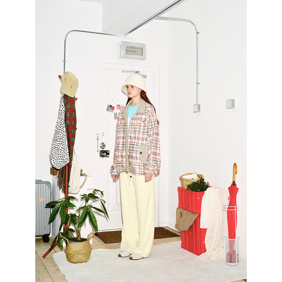 Model wearing a pastel plaid zip jacket with gray trim and patch pockets, cream wide-leg pants, and a white bucket hat.