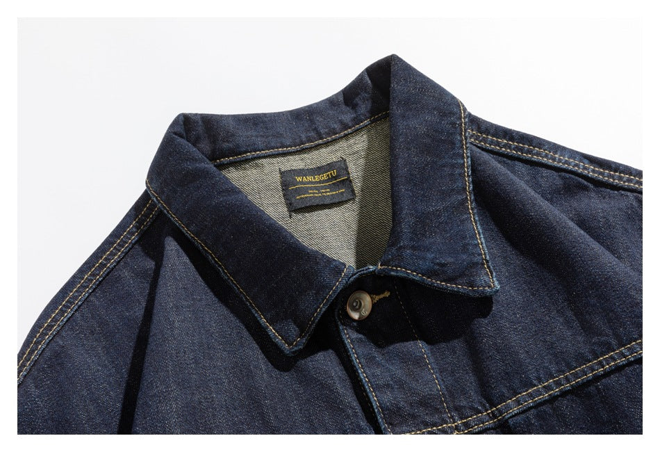 Close-up of a dark indigo denim jacket collar, neck label, and golden contrast stitching.
