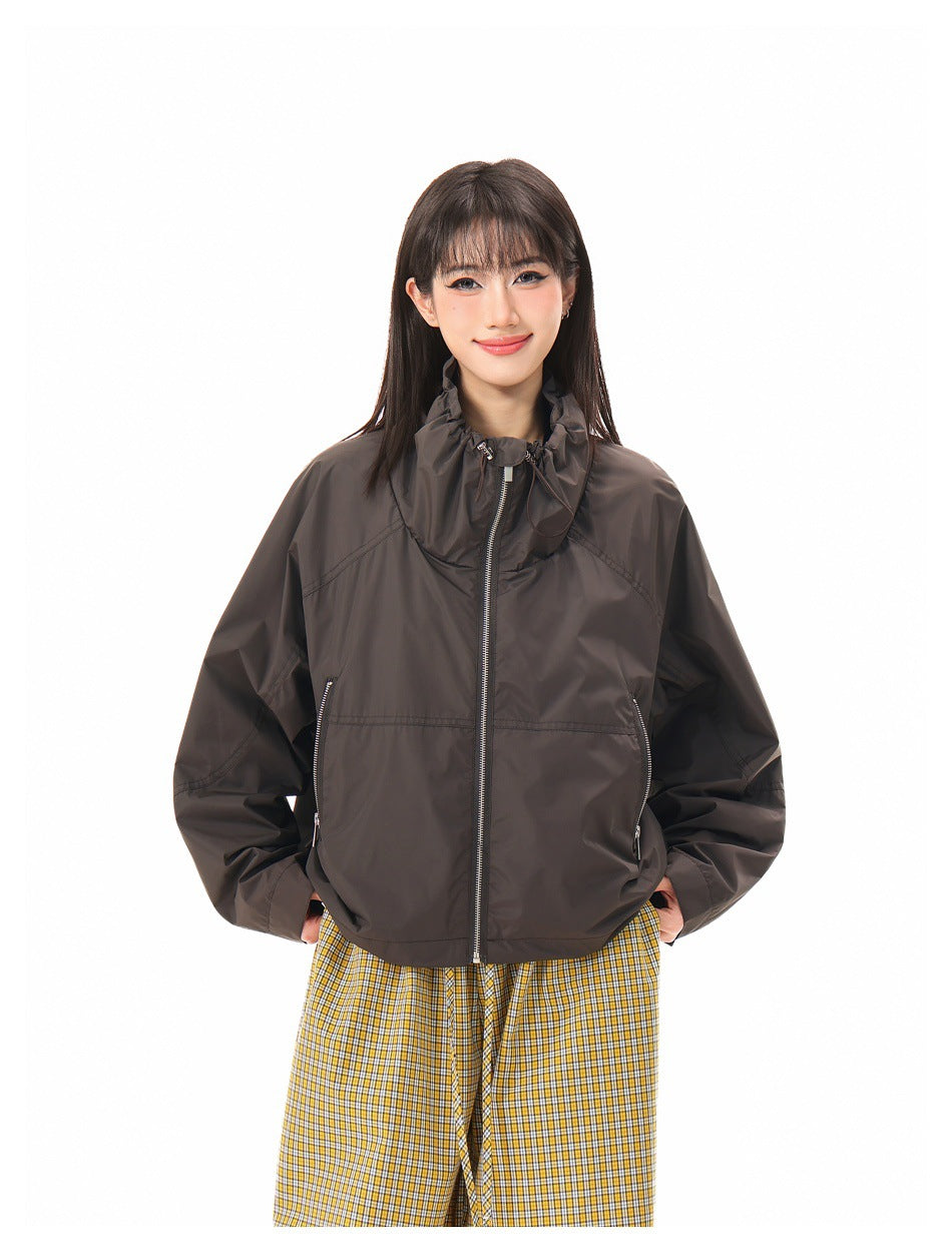 Closer front view of a model wearing a dark brown jacket with a gathered collar, center zip, and zippered pockets.