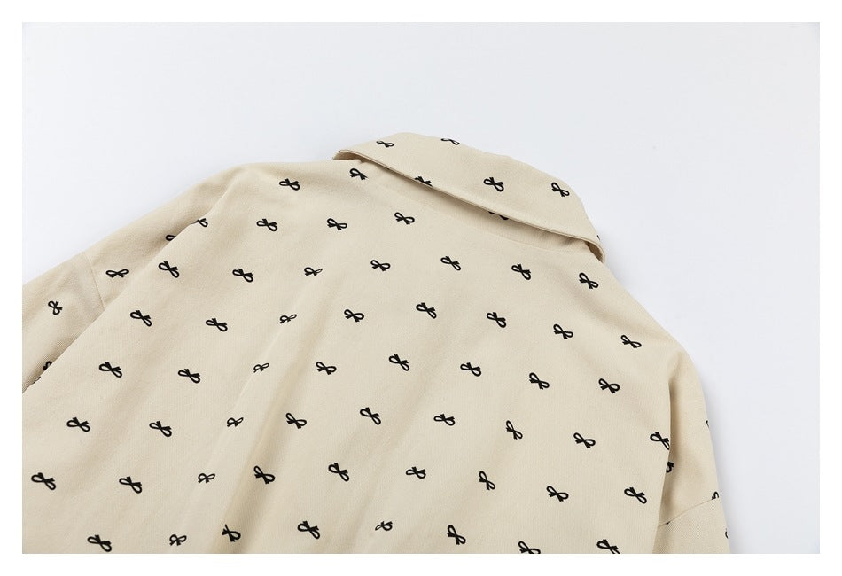 Back of a beige collared garment with an all-over pattern of small black bows, laid flat.