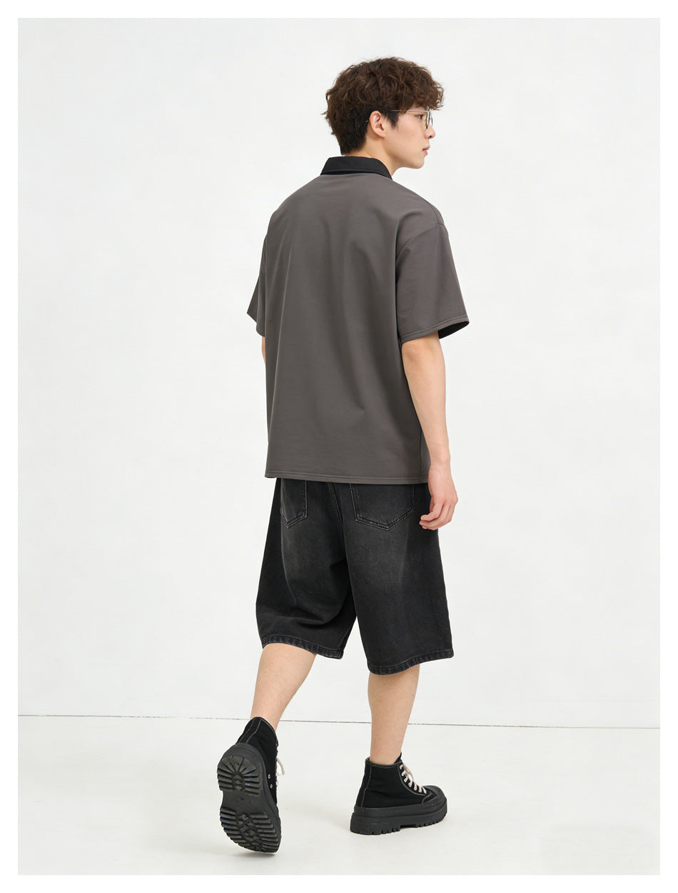 Rear view of a model wearing a charcoal polo with black collar and loose black denim shorts.
