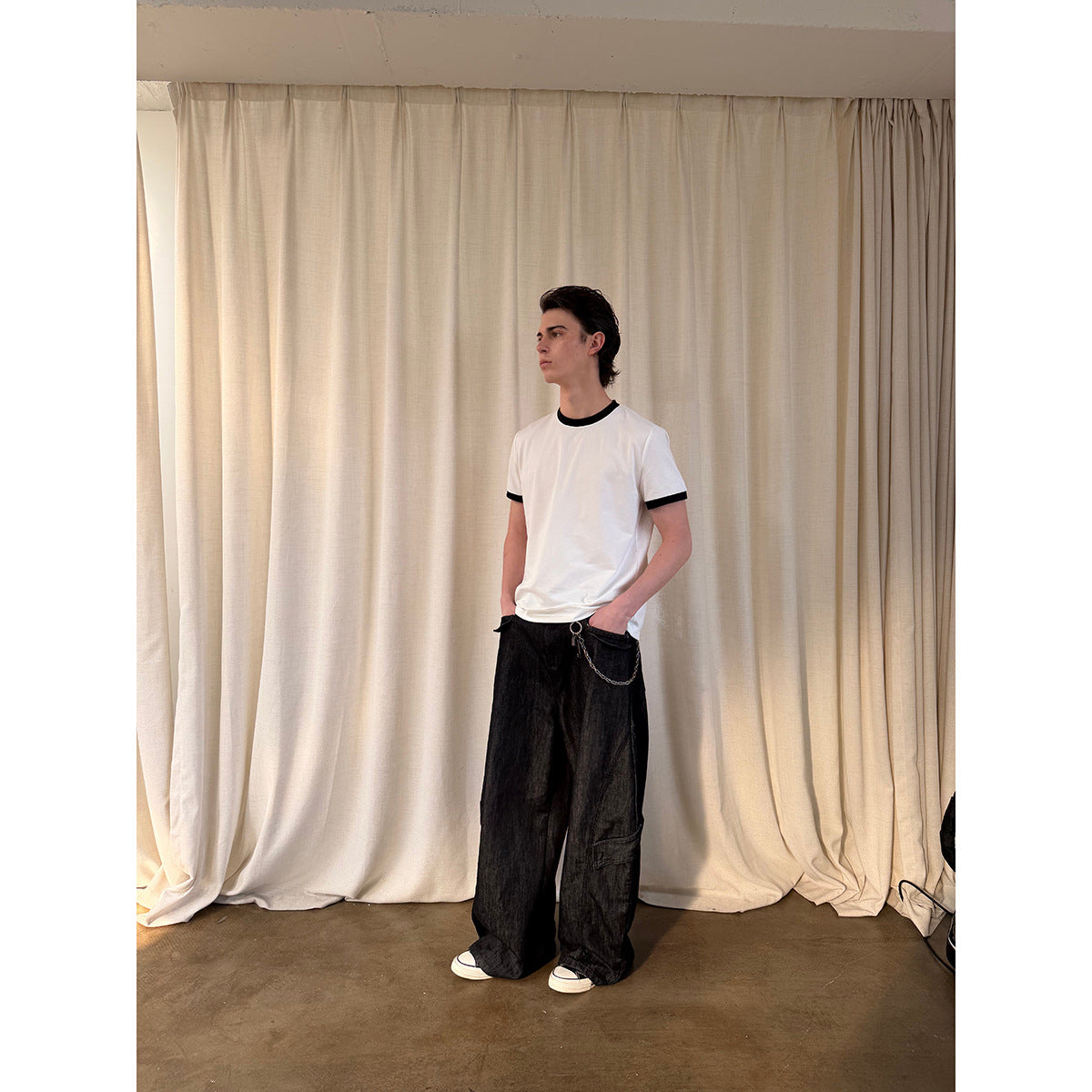Full-length model wearing a white T-shirt with black ribbed collar and sleeve bands, paired with loose black pants.
