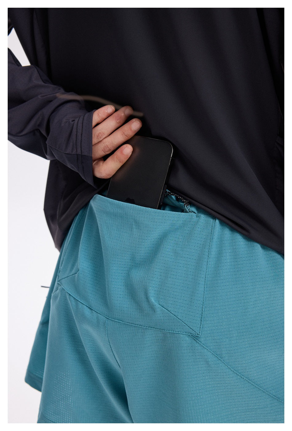 Close-up of turquoise running shorts as a phone is placed into the large rear pocket.