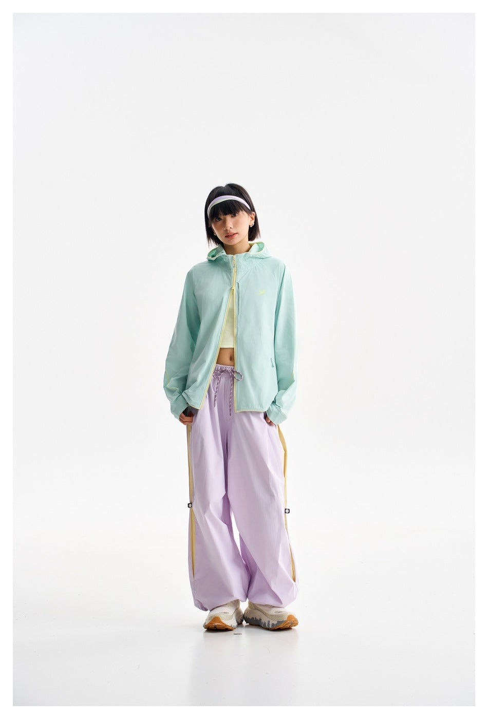 Model wearing a mint hooded zip jacket and loose lavender pants, shown from the front.