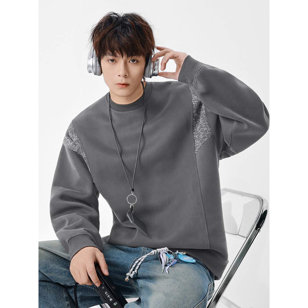 Model wearing an oversized charcoal gray crewneck sweatshirt with textured gray shoulder panels and ribbed cuffs.