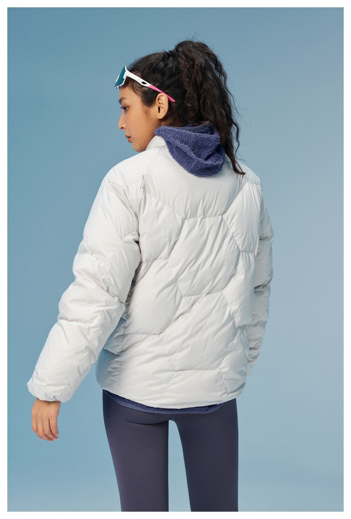 Rear three-quarter view of a woman wearing a white quilted puffer jacket with a navy fleece-lined collar.