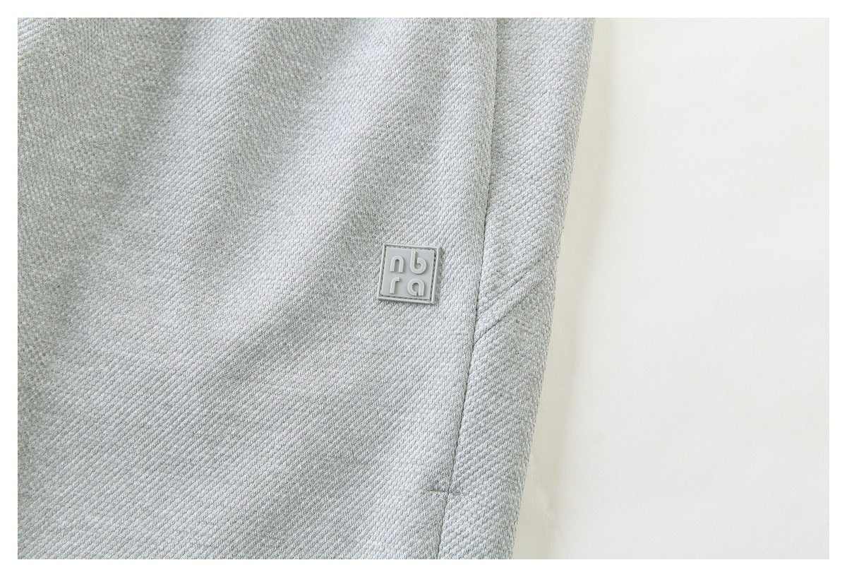 Close-up of pale gray textured garment fabric with a small raised square logo patch.