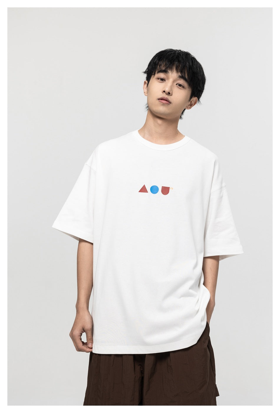 Front view of a model wearing a white T-shirt with a small red and blue geometric chest graphic.