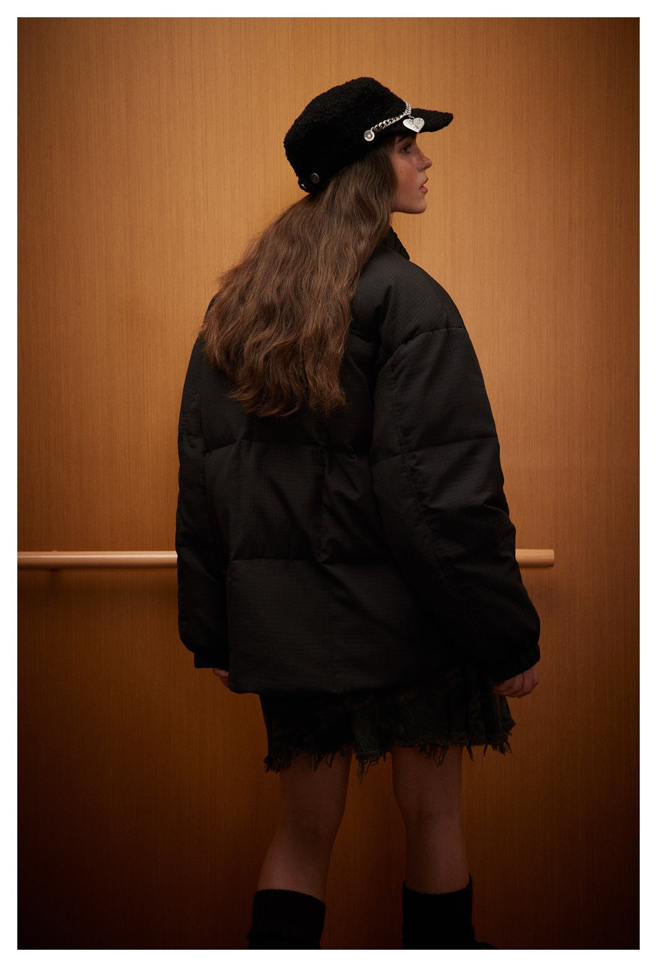 Model viewed from behind wearing a black oversized puffer jacket and black cap.