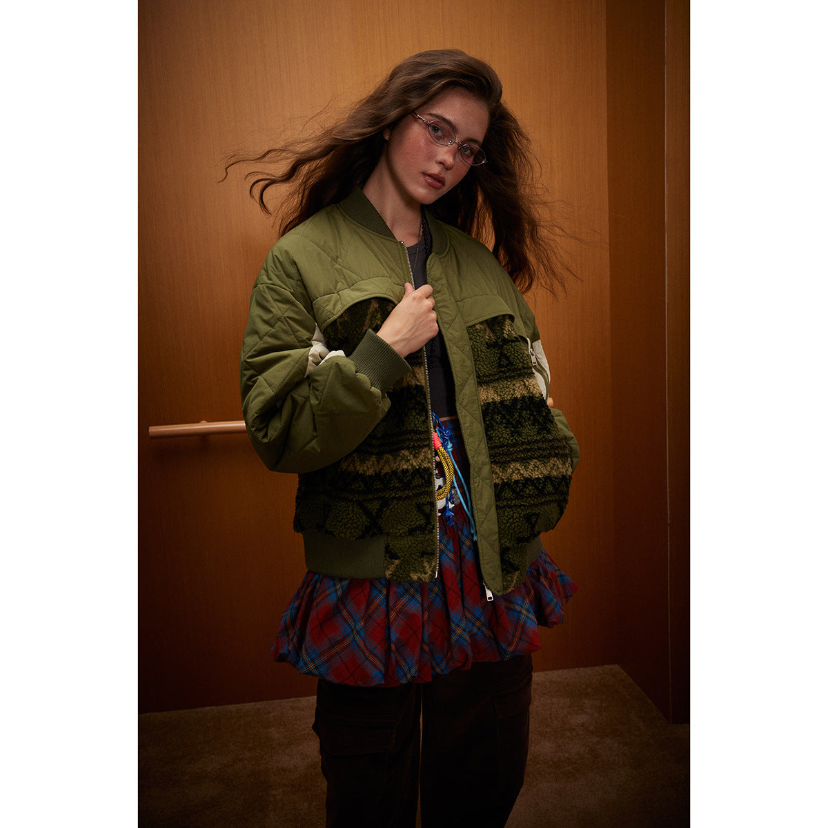 Model wearing an olive quilted bomber jacket with a dark patterned body, cream sleeve panels, and ribbed trim.