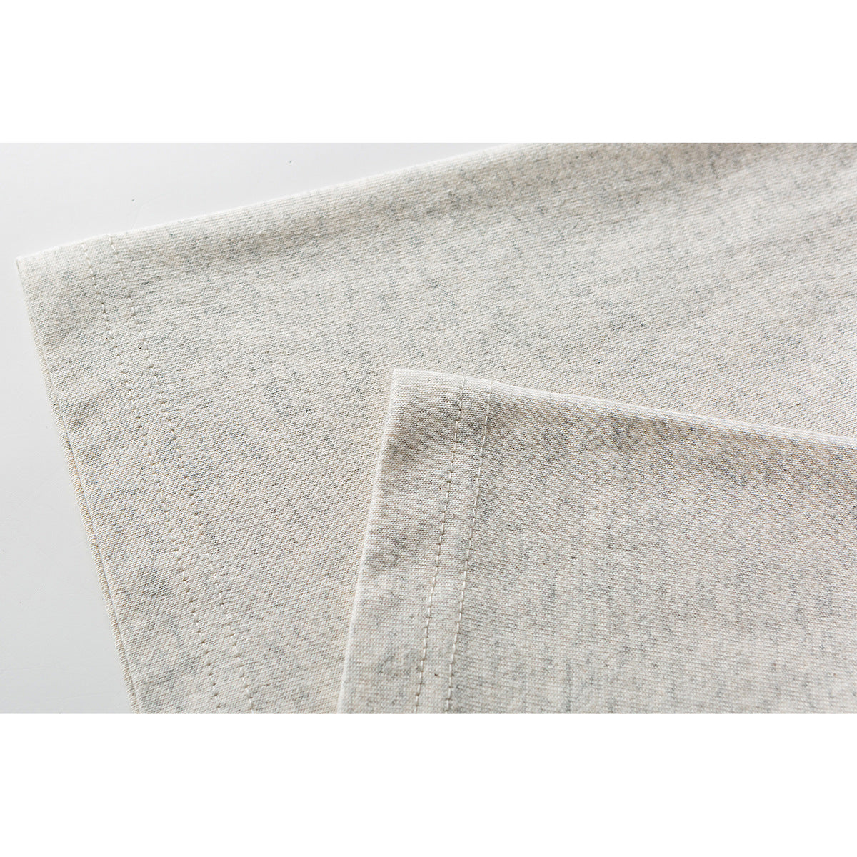 Close-up of light heather gray fabric showing double-stitched garment hems.